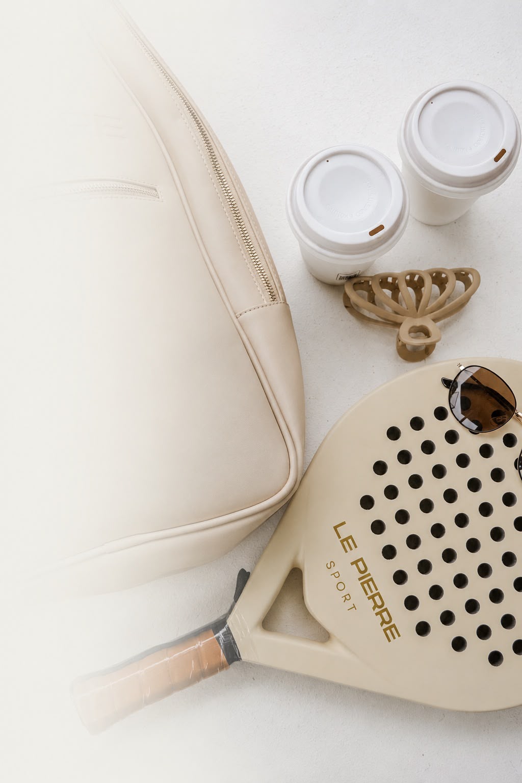 Flatlay of Le Pierre Sport bag, coffee cups, scrunchie, sunglasses and padel racket